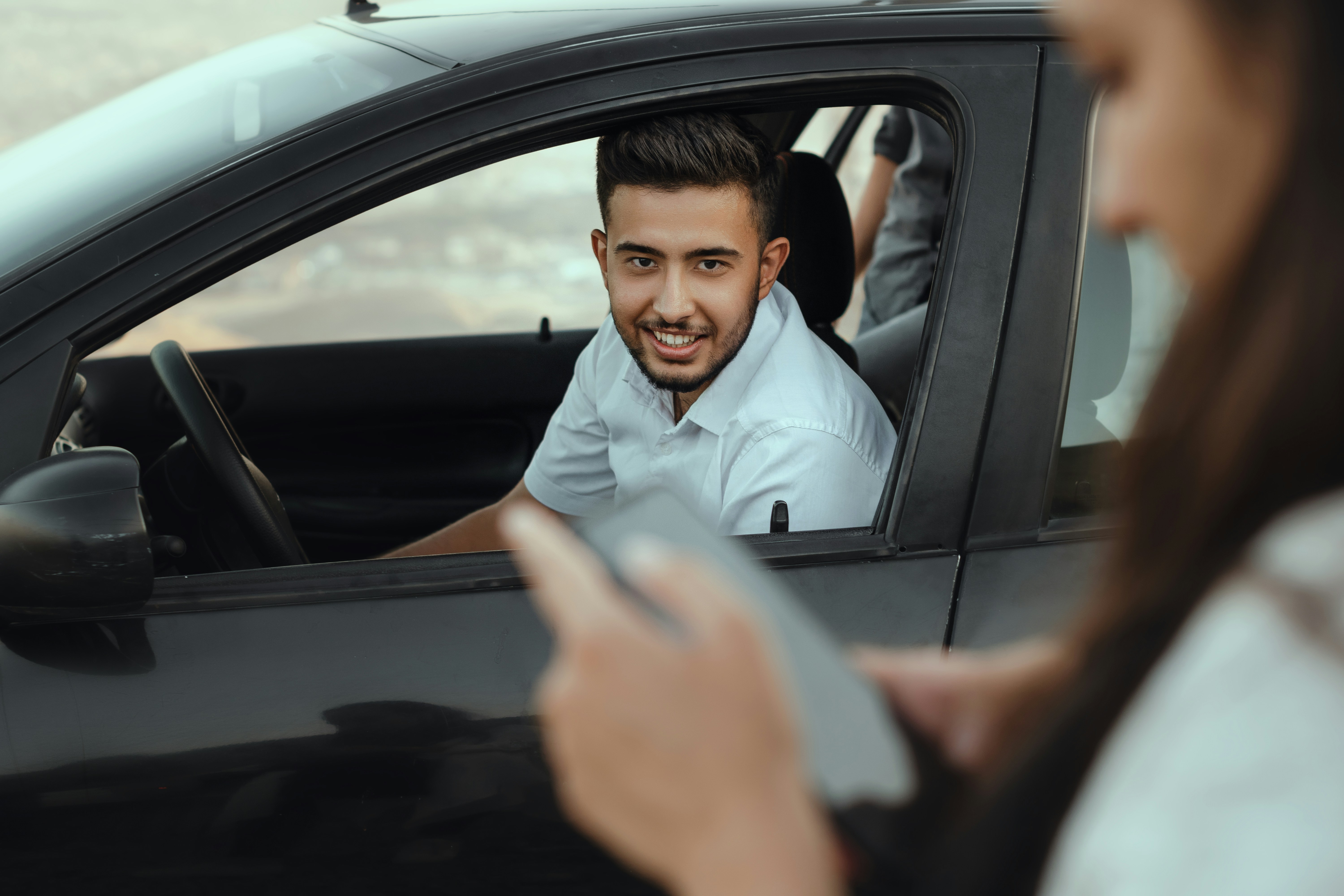 Un chauffeur souriant accueille chaleureusement sa cliente à travers la vitre du véhicule — photographie d'illustration